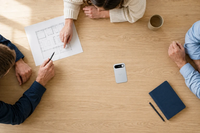 Overhead view of a team discussing a floor-plan sketch, with the approved Silver Audream Note Pro front on the desk.